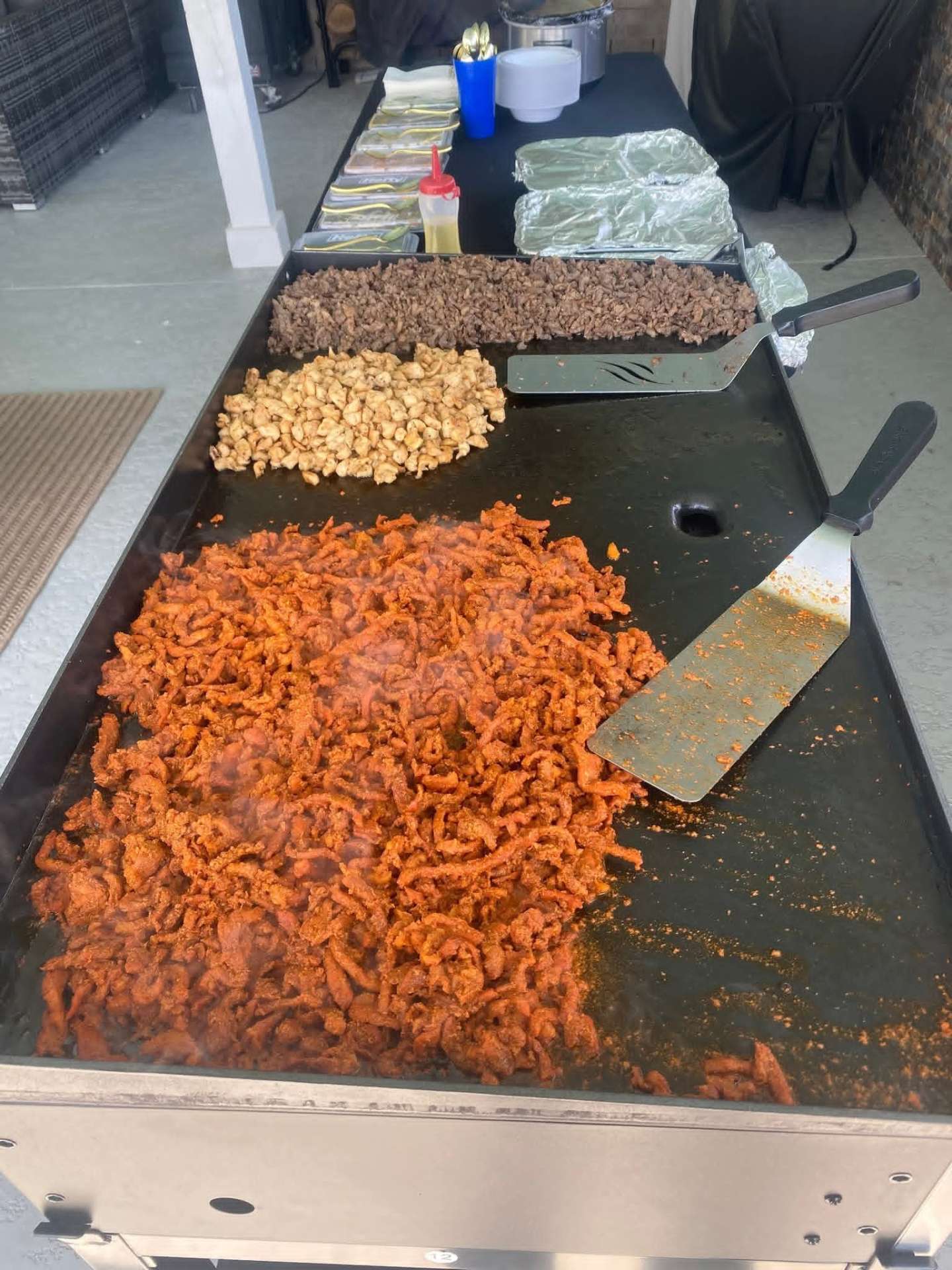 Beef, chicken and al pastor cooking on the flat-top grill